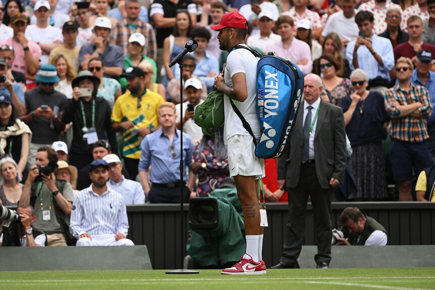 Nick Kyrgios carries his tennis bags while being interviewed on court at Wimbledon.