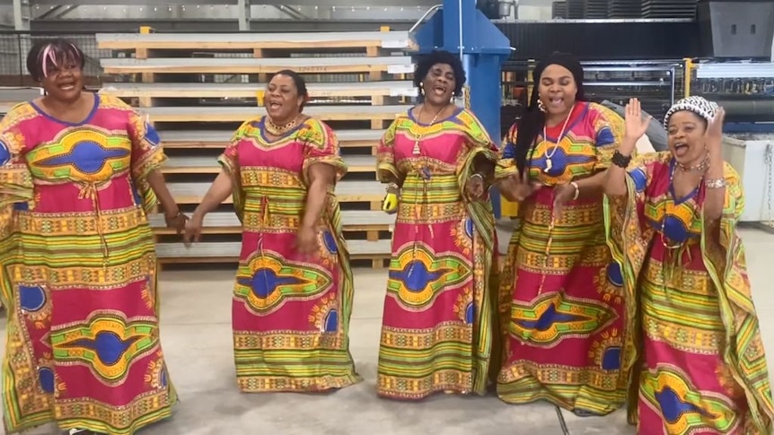 A group of Congolese women in colourful clothes dance and sing in a factory