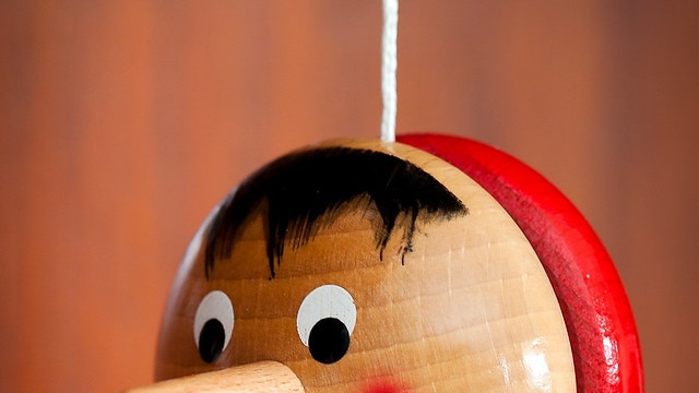 A wooden yoyo painted to look like Pinocchio is suspended in mid-air, set against a blurred brown background.