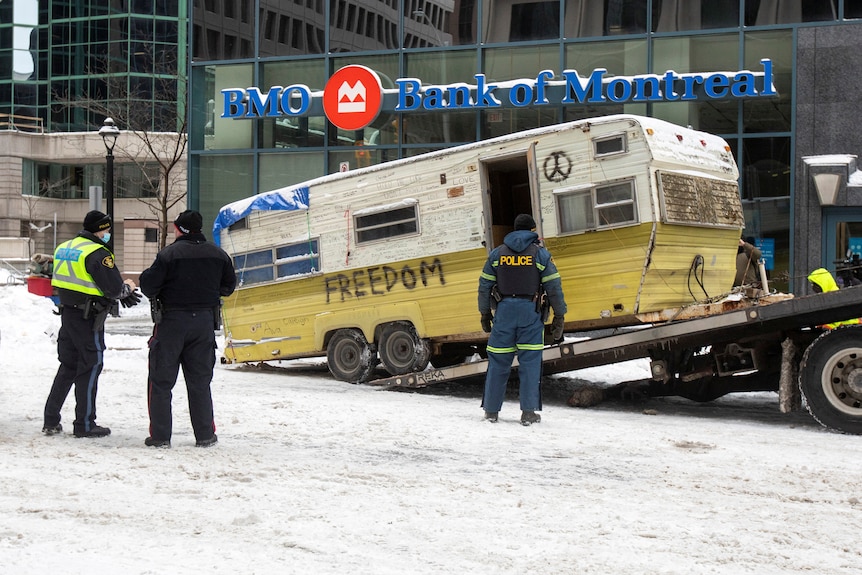 A rusted campervan with the word 'freedom' spray painted on the side is loaded onto a tow truck by authorities