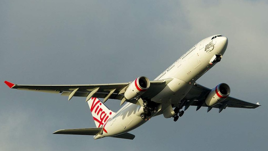 A Virgin plane flies in the sky. It is tilted upward after taking off.