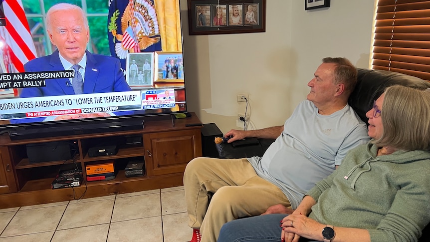 A middle aged couple watch Fox News coverage of the aftermath of the Trump shooting in their living room.