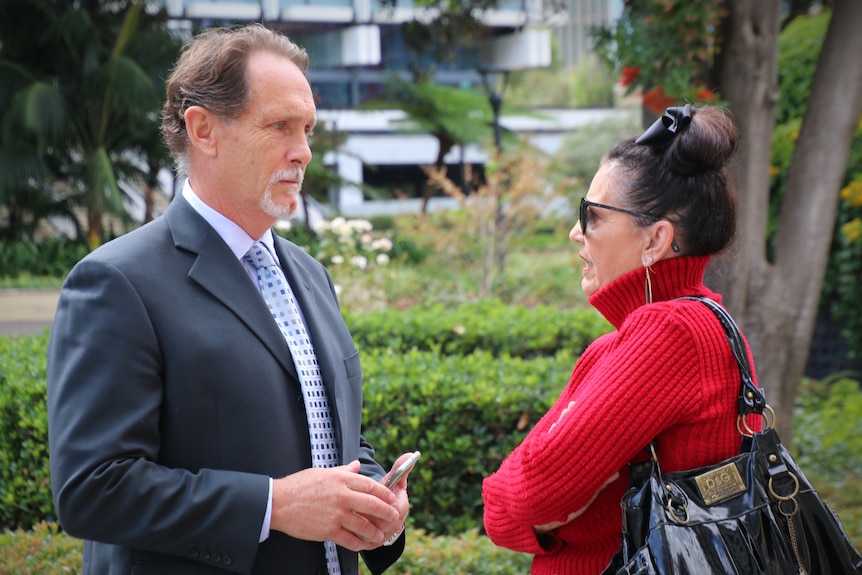 A man in a suit and tie speaks with a woman wearing a red cardigan