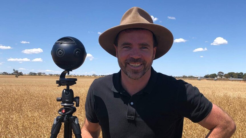 Tim Gentle stands beside his 360-degree camera in a field.