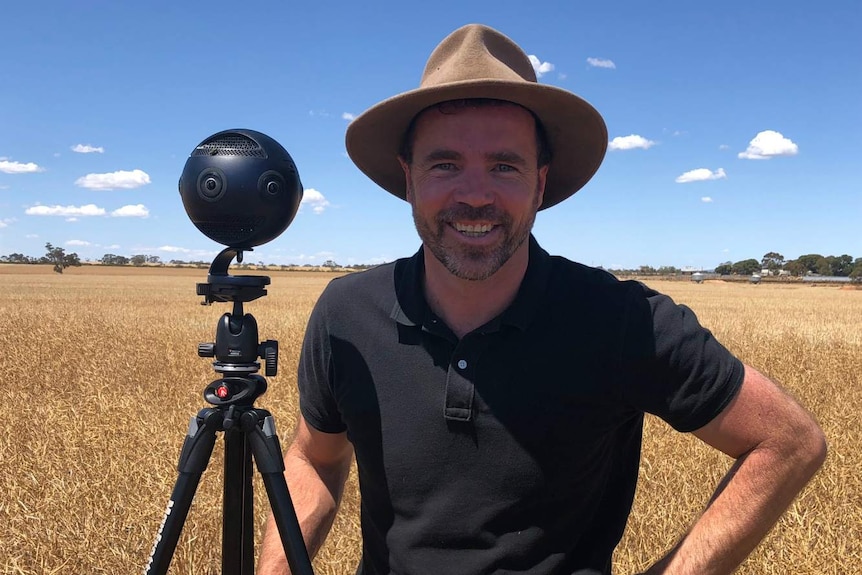 Tim Gentle stands beside his 360-degree camera in a field.