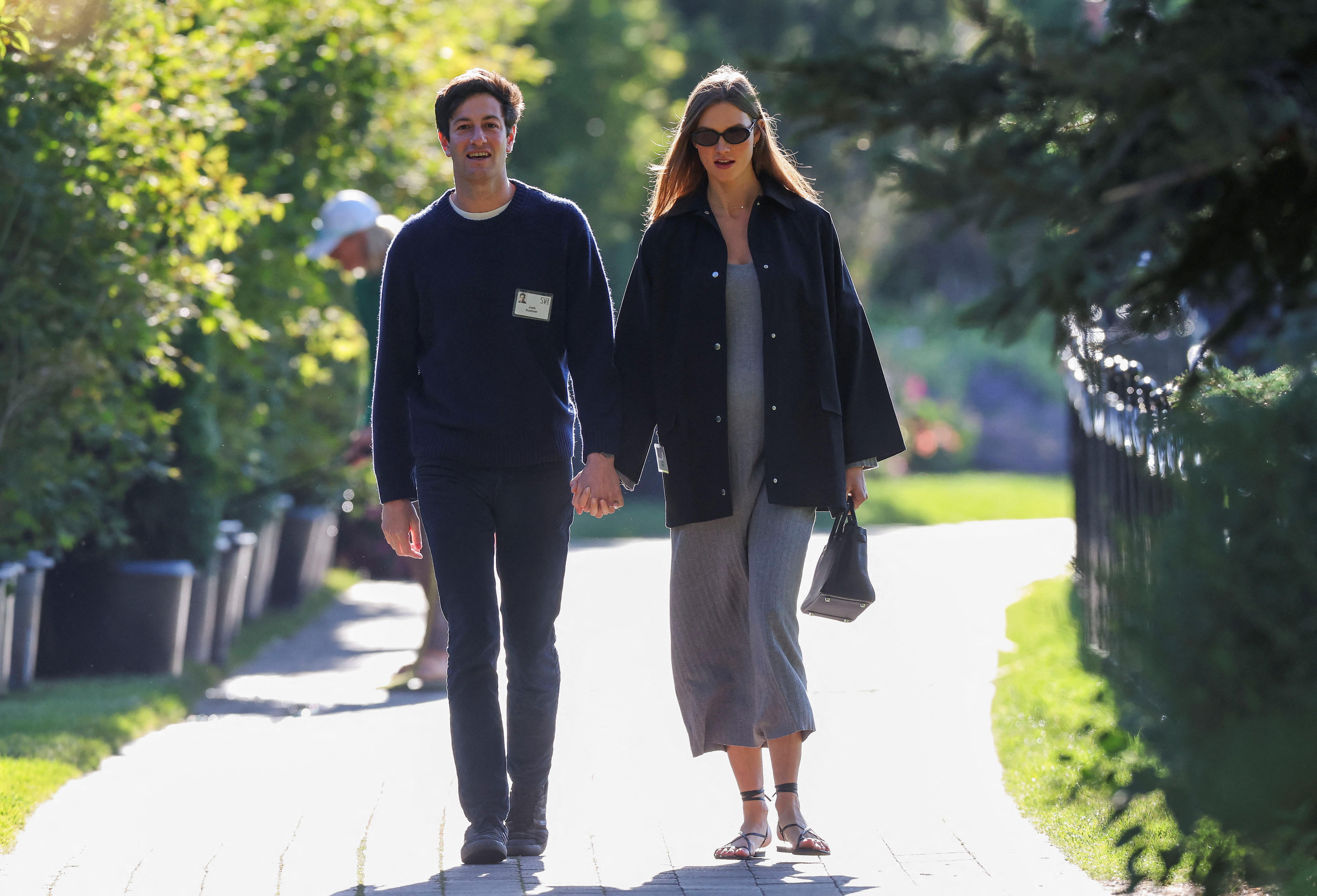 A dark-haired man and woman walk hand in hand along a footpath in a park.