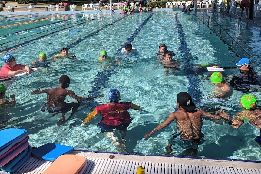 Group of adults in a circle in the pool some with heads in the water blowing bubbles