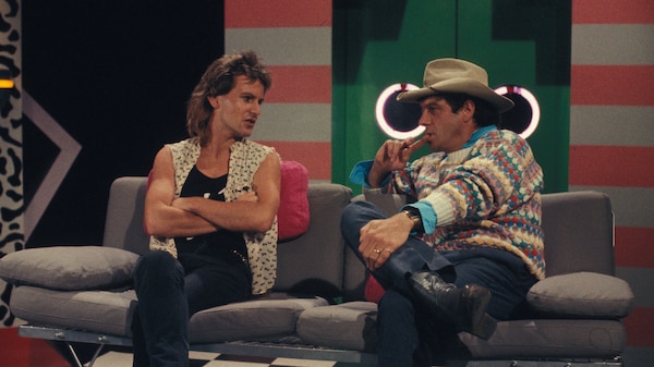 Two people sitting down on a couch in a studio from the 1980s