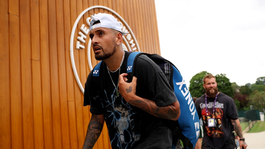 Nick Kyrgios walks with a bag on his back as he passes a sign for 'The Championships' at Wimbledon.