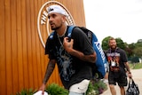 Nick Kyrgios walks with a bag on his back as he passes a sign for 'The Championships' at Wimbledon.