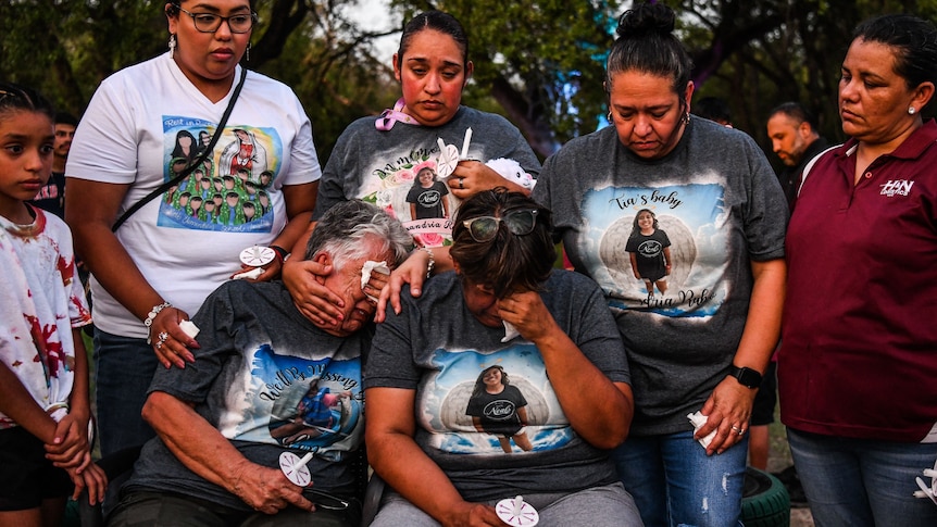 A group of people, some wearing shirts featuring the photo of a young girl, hold candles and weep.