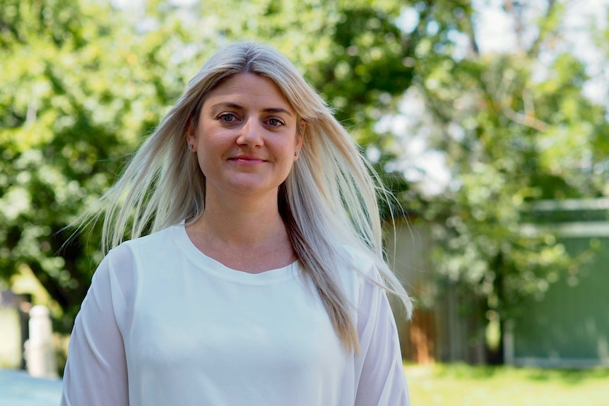 A woman smiles in front of a bush