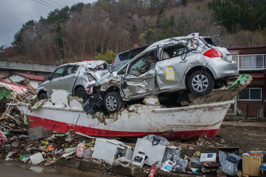 Damaged cars on top of a boat and piles of rubbish.