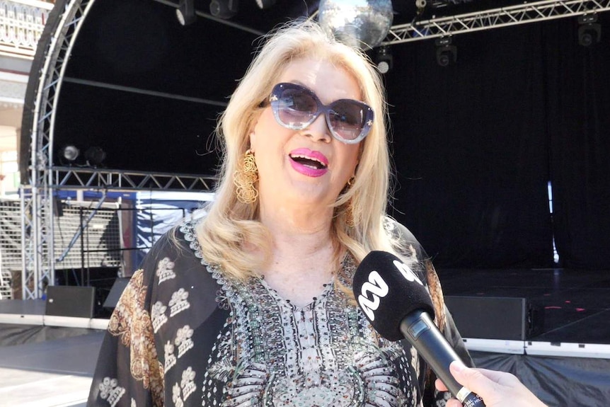 A woman smiles talking in to a microphone.