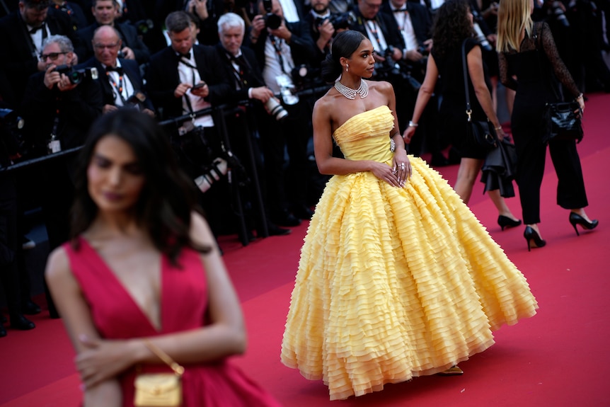 Lori Harvey wearing a strapless yellow gown with a full skirt with small ruffles cascading down. 