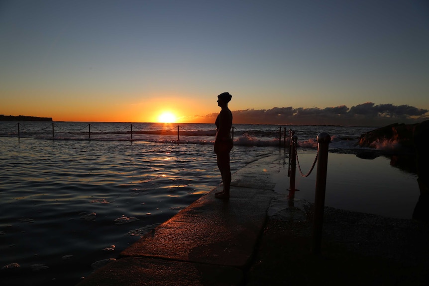 Portrait of a girl standing by the edge of an ocean bath in her togs on sunrise.