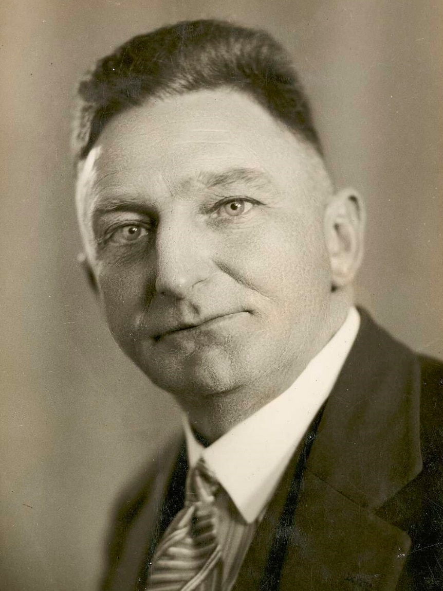 A 1930s sepia photo of a dapper-looking man, who is staring directly into the camera