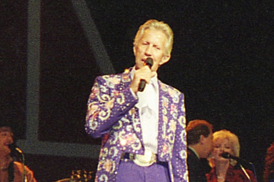 Porter Wagoner singing on stage wearing an elaborately embroidered suit.