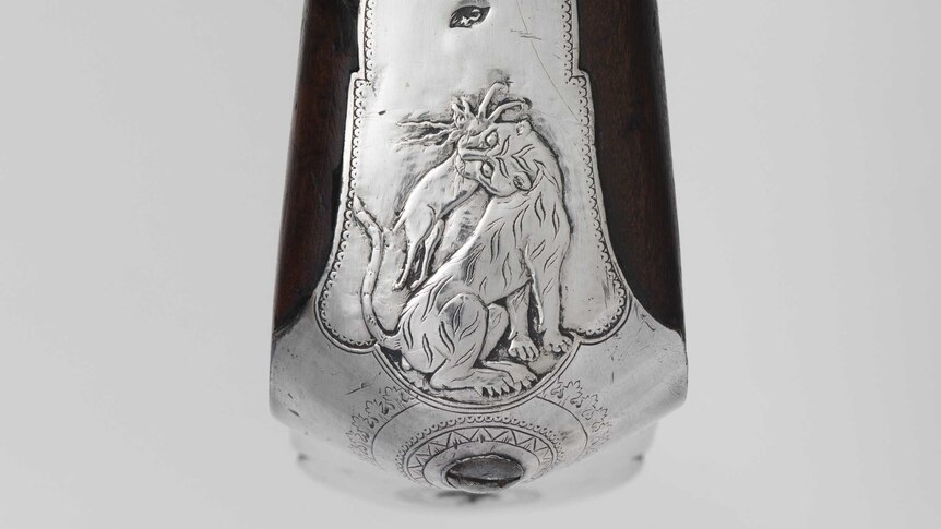 A tiger eats a deer in a decorative silver plate attached to the wooden butt of a rifle.