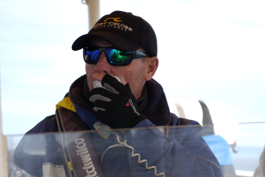 A man with sunglasses and a hat talking into a two-way radio aboard a boat