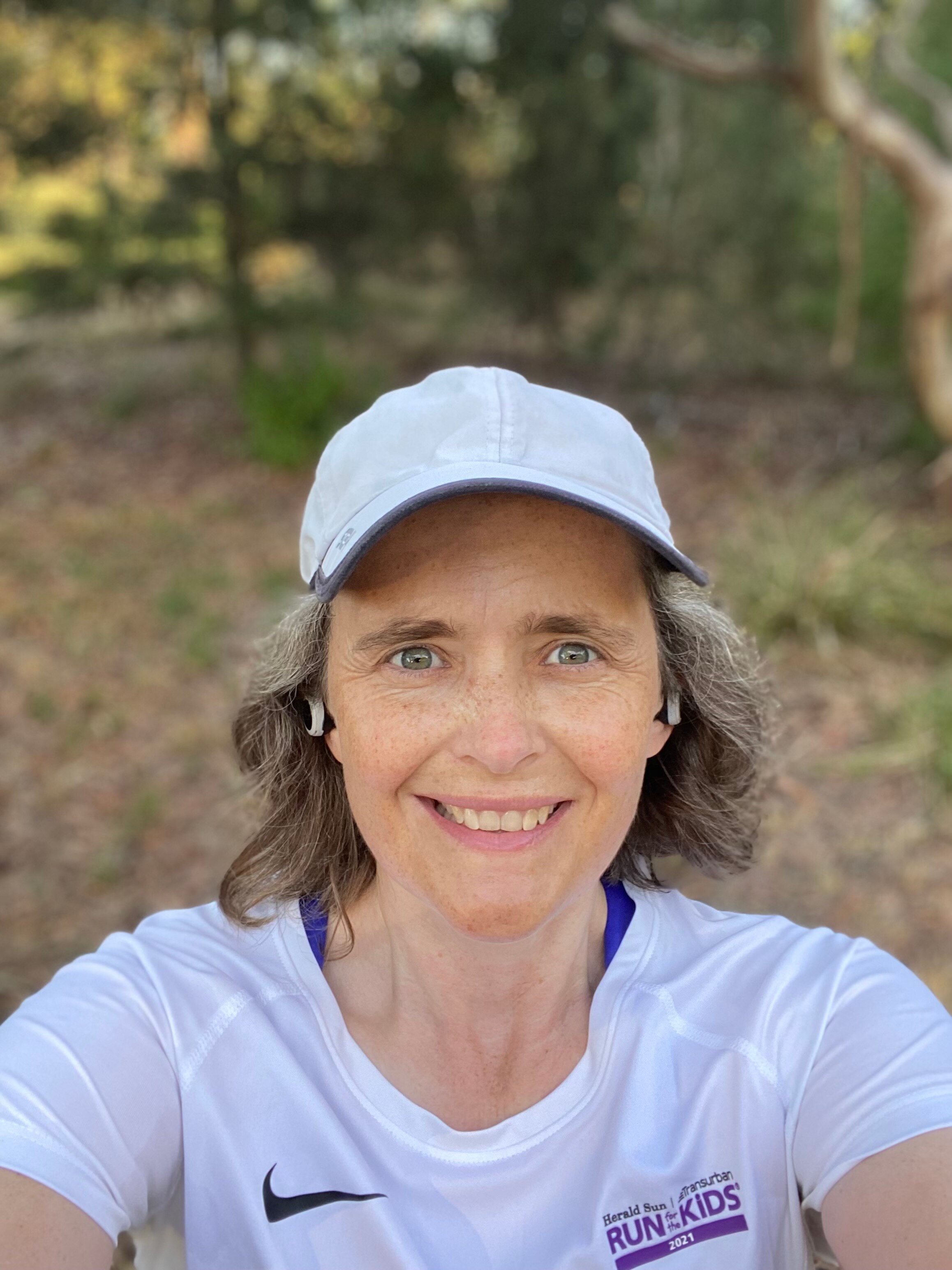Selfie of a middle-aged woman in white cap and tshirt, stopping mid-run to smile.
