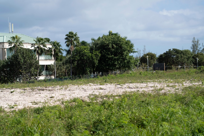 A vacant block of land with grass and a large section of dirt. 