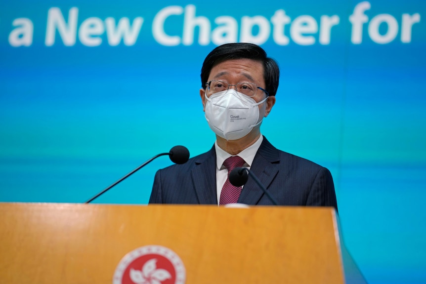 Un homme portant un masque se tient derrière un podium et parle dans un microphone