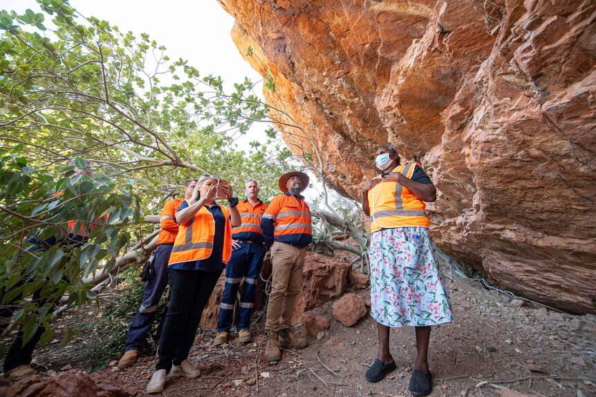 A woman stands with a group of people in high-vis vest under a rock overhanging.