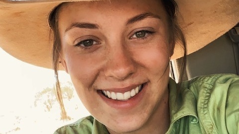 A lady in a green work shirt and a light brown Akubra hat with black sunglasses resting on the brim.