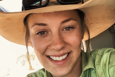 A lady in a green work shirt and a light brown Akubra hat with black sunglasses resting on the brim.