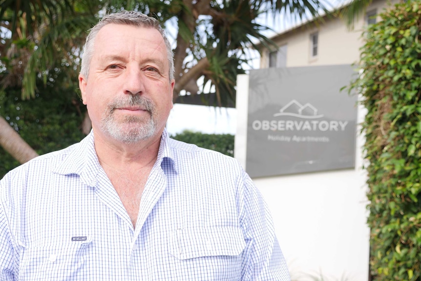 A man with a serious face stands next to an accommodation sign