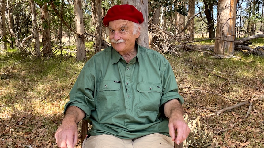 A man sitting on a chair with trees behind him looking at the camera