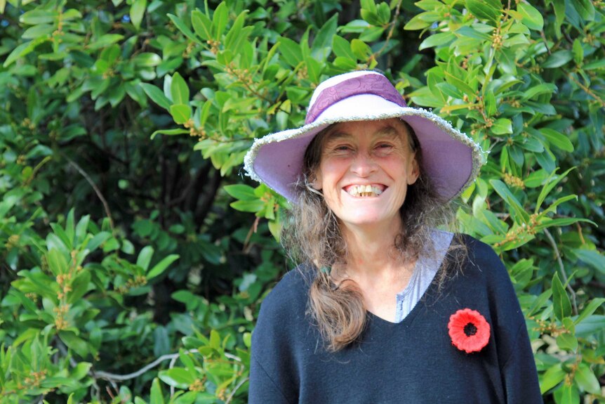 Woman in a purple hat smiling in front of a large bay tree