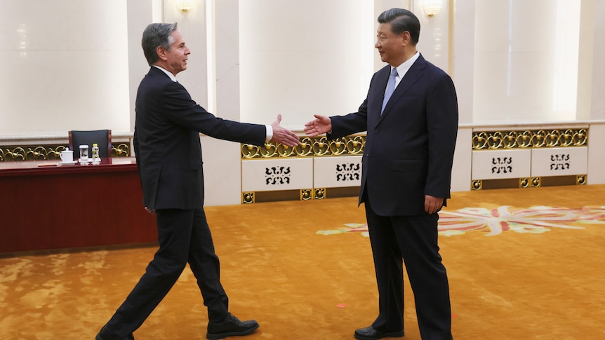 A western man extends his hand and walks towards a taller Chinese man in a conference room