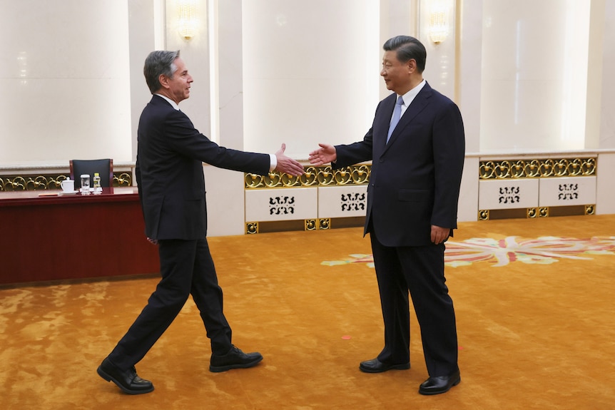 A western man extends his hand and walks towards a taller Chinese man in a conference room