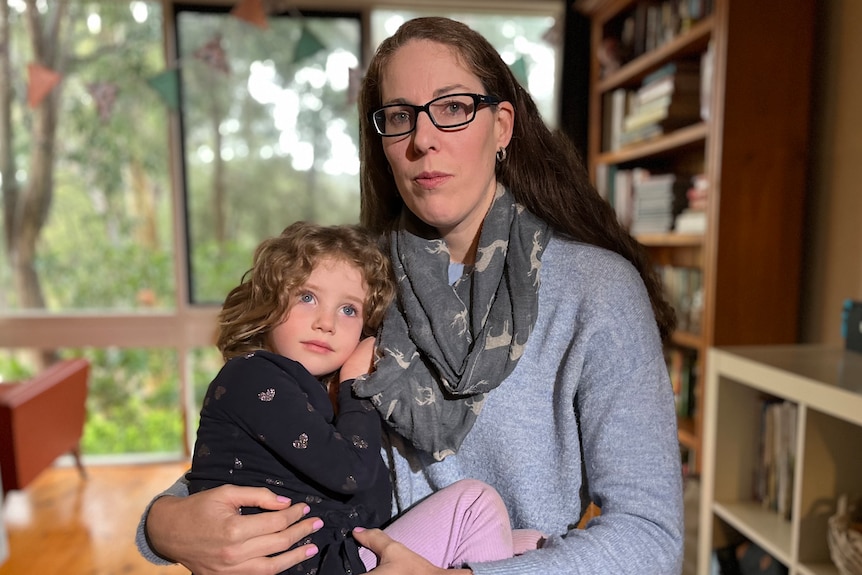 Laura wearing a grey jumper, holding her four-year-old daughter in her arms.