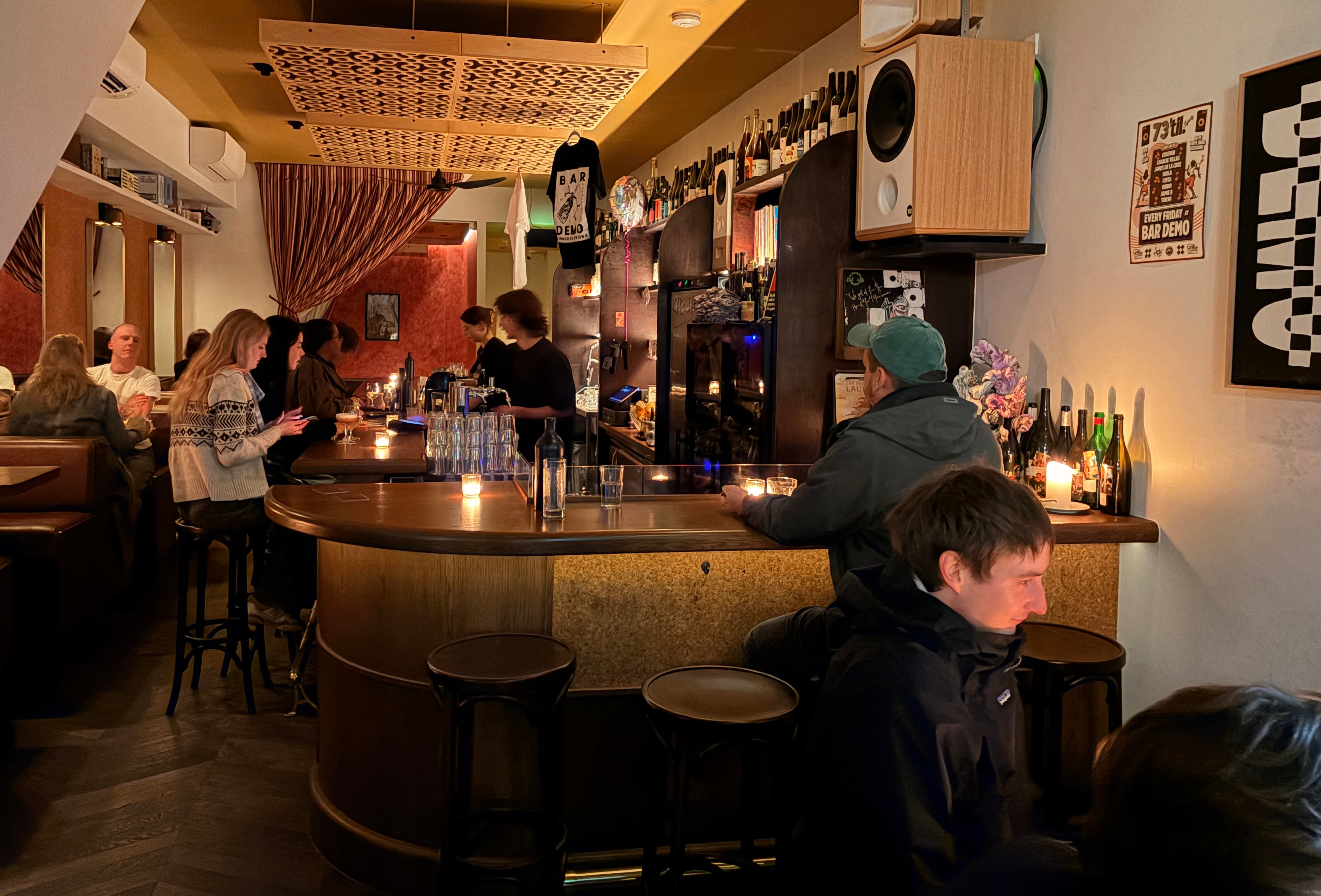 Poeple sit at tables and bar in dimly lit bar