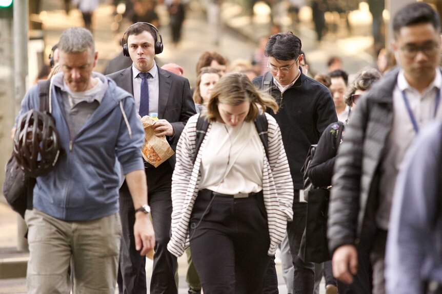 Commuters with their heads down on a crosswalk.