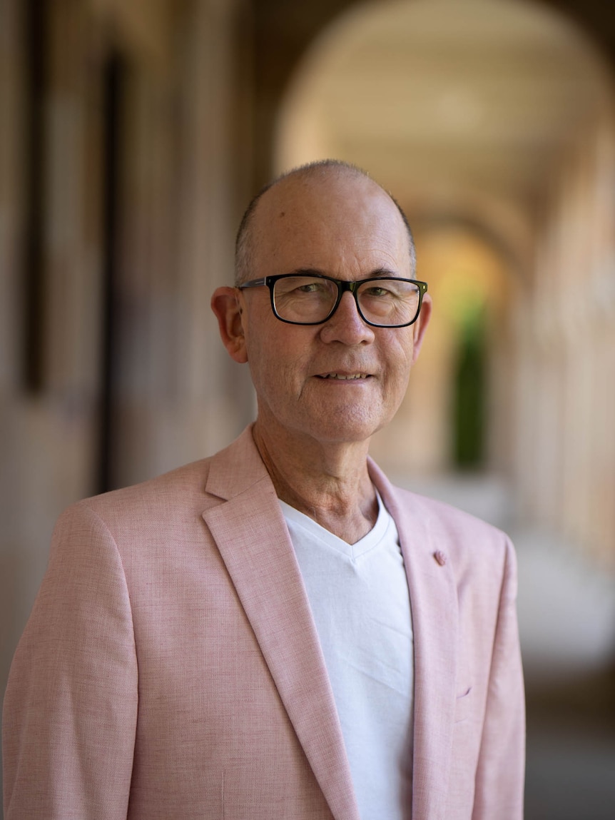 A portrait of a man in a suit jacket with a sandstone university in the background