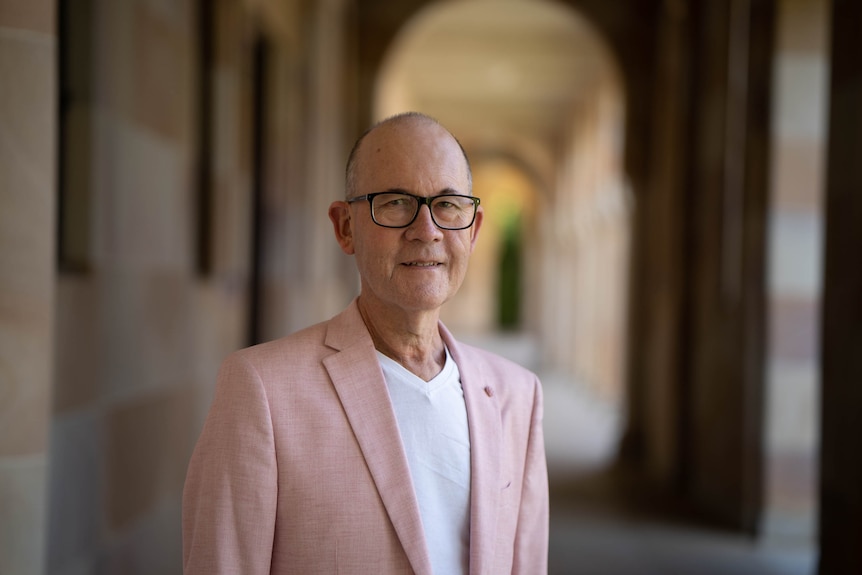 A portrait of a man in a suit jacket with a sandstone university in the background