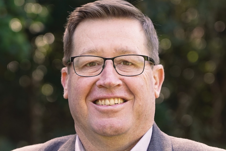 A man wearing a suit jacket and glasses smiles at the camera