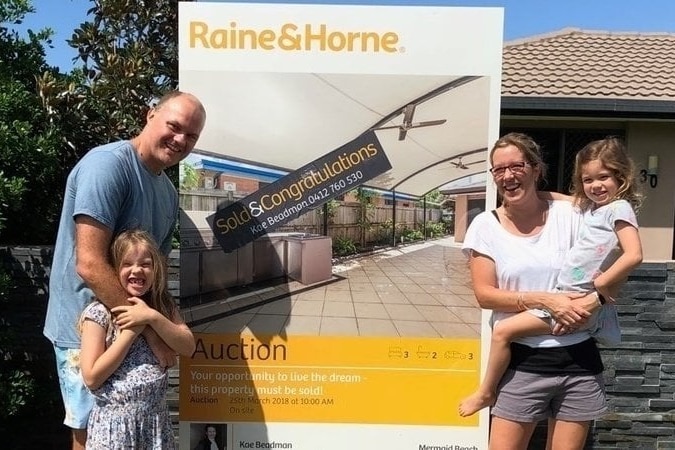 A couple stand next to an auction sign with two kids