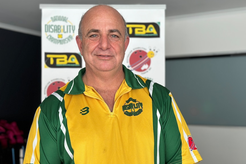 A man smiling, wearing a green and gold polo shirt that says 'National Disability Championships'.