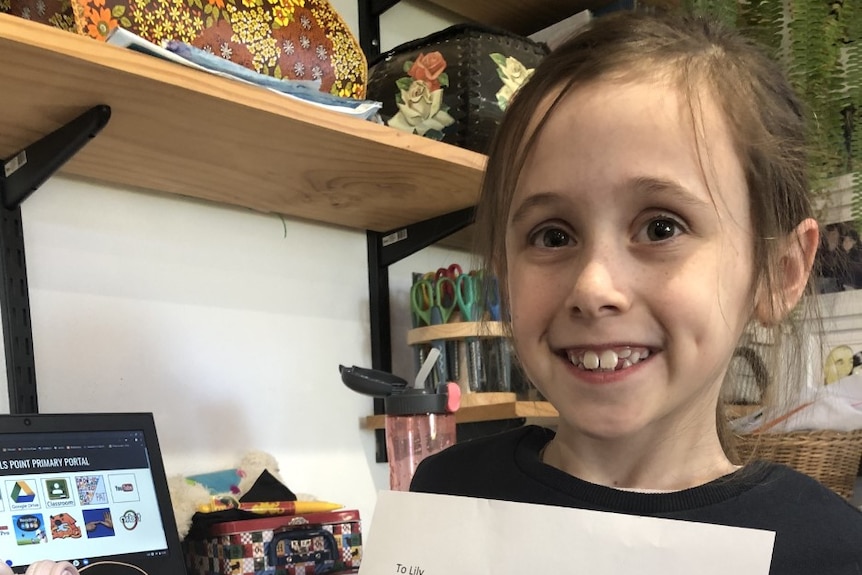 girl smiling holds up letter while sitting at desk.