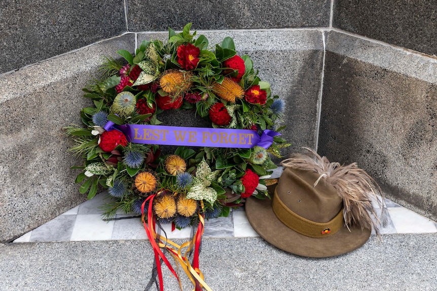 A green wreath featuring bottlebrush flowers and a veterans hat with the Aboriginal flag pinned on it 