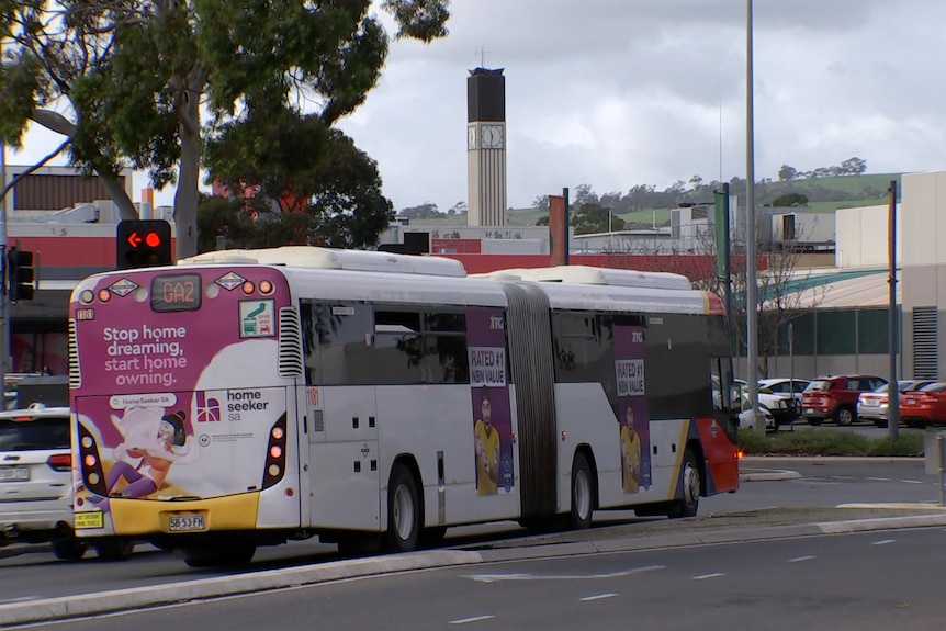 An articulated bus drives towards a shopping centre