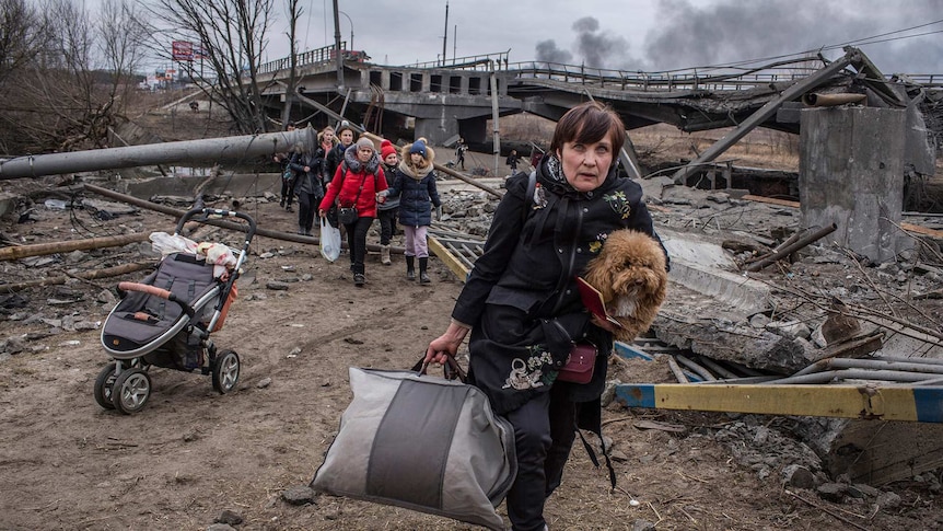 Ukrainian refugees walking through rubble with their belongings.