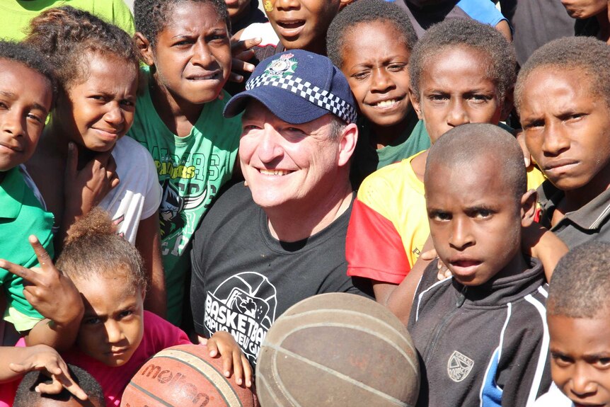 An Australian man in a police cap surrounded by children and basketballs.