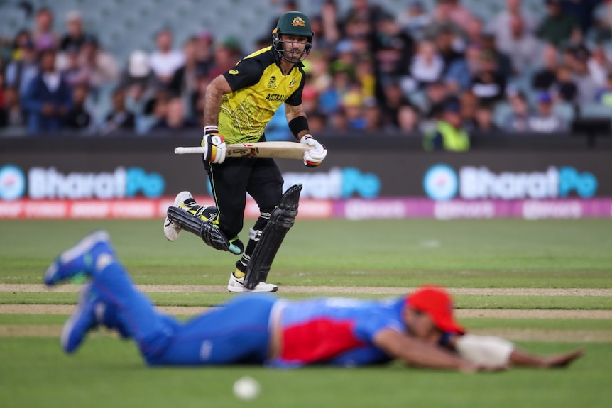 Glenn Maxwell runs as an Afghanistan fielders dives, blurred in the foreground