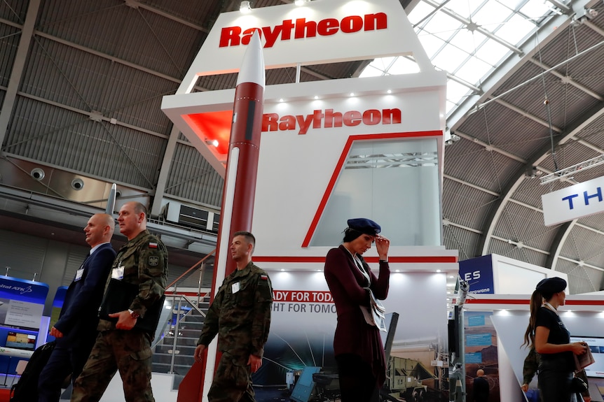 People pass the US defense company Raytheon stand at a military fair.